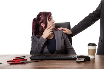 Woman sitting at work desk with someone elses hand on her shoulder - Types of Sexual Harassment